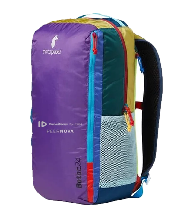 Cotopaxi Batac 24L Daypack in purple Del Día colors with the Cuneiform for CRM and PeerNova logos on the front